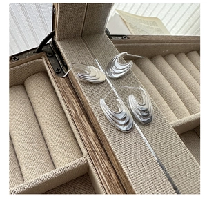 Detailed view of layered curved silver earrings displayed in a wooden jewelry box