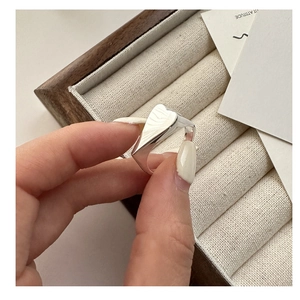 Detail of a hand holding a polished silver heart signet ring over a wooden jewelry box