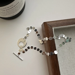 Collier minimaliste en argent S925 avec sequins et fermoir OT posé sur cadre en bois
