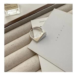 Macro detail of minimalist heart ring on beige tray showing adjustable silver open band