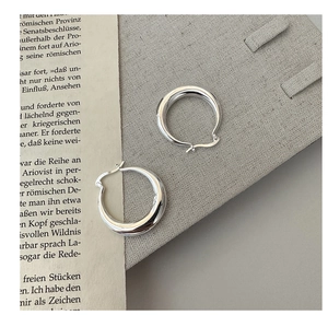 Détail macro des boucles d'oreilles créoles larges en argent S925 poli sur fond texturé