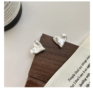 Detailed close-up of textured heart-shaped S925 sterling silver stud earrings on wood