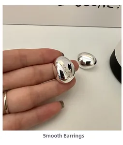 Close-up of polished S925 sterling silver oval stud earrings held in hand