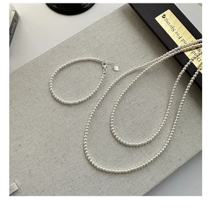 Close-up of a 925 silver double-layer pearl necklace and bracelet set on grey fabric