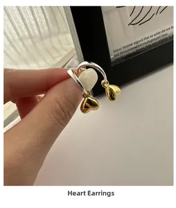 Dettaglio di orecchini a cerchio in argento con ciondoli a cuore d'oro in mano
