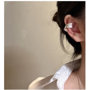 Détail macro de boucle d'oreille minimaliste en argent mat portée sur l'oreille