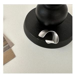 Vue détaillée d'un clip d'oreille ondulé en argent mat sur un support noir élégant