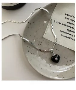 Detail of a minimalist black heart pendant on a flat silver snake chain with vintage style