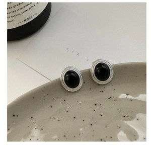 Close-up of S925 silver black onyx oval stud earrings on a textured ceramic dish