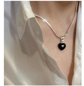 Close-up of a S925 silver heart necklace with black drip oil pendant on white shirt