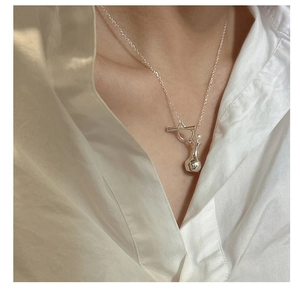 Detail of S925 silver necklace with perfume bottle pendant worn on a white shirt