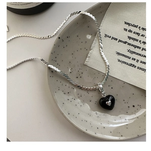 Detail of a black enamel heart pendant on a silver snake chain over a rustic ceramic plate