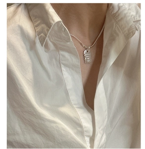 Macro view of textured square silver pendant on a delicate snake chain necklace