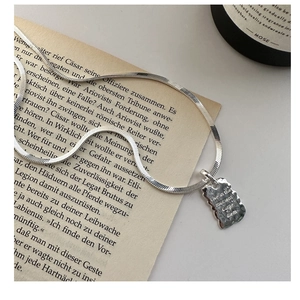Macro detail of S925 silver necklace with engraved rectangular pendant on vintage paper
