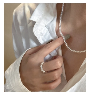 Detail of silver S925 square stone necklace and fluid lava ring on a model in white linen
