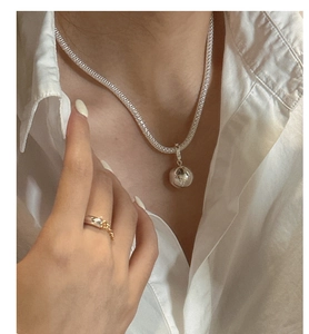 Detailansicht eines Silberkugel-Anhängers an einer strukturierten Kette im Minimal-Stil