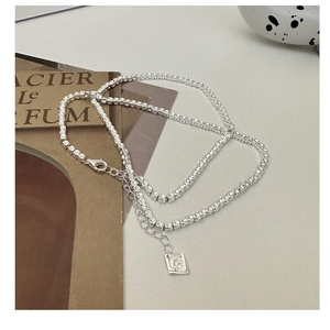 Detail of S925 sterling silver square bead necklace with lobster clasp and tag on sand texture