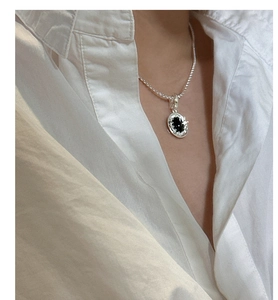 Detail of silver wavy pendant with black agate on a delicate chain worn with a white shirt