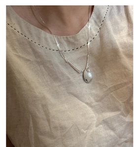 Detail of S925 sterling silver bean pendant necklace worn on a casual linen shirt