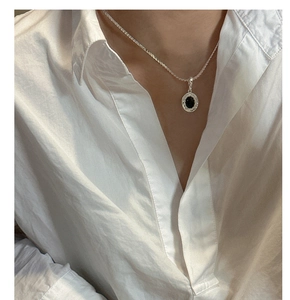 Close-up of S925 silver wavy necklace with black onyx pendant on a white shirt