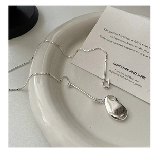 Close-up of S925 sterling silver bean pendant on a ceramic tray with minimalist card