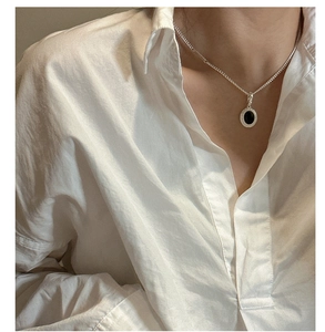 Close-up of S925 silver necklace with oval black agate pendant on white fabric