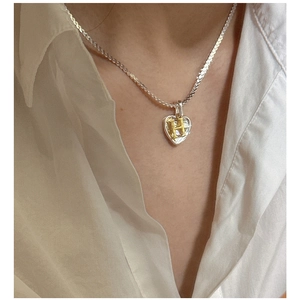 Detail of silver snake chain and heart pendant with golden letter H on white linen