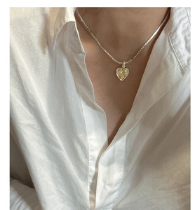 Detail of S925 silver heart pendant with golden H letter on flat herringbone chain