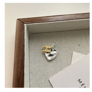Macro shot of silver heart pendant with gold H letter on a textured linen tray