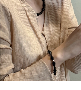 Detail of s925 silver beaded necklace with black onyx teardrops on a beige shirt