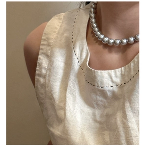 Détail d'un collier à perles argentées avec une veste en lin aux coutures noires à la main