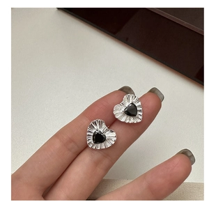 Detailed view of silver heart stud earrings with black zircon and pleated texture