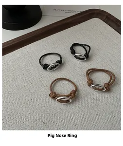 Detail of woven cord pig nose rings in black and brown on a minimalist linen display