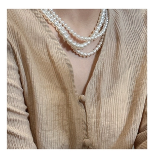 Détail d'un collier de perles à trois rangs porté sur une chemise plissée beige