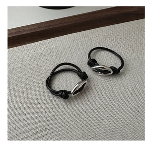 Detail of minimalist black woven rope bracelet with silver oval hollow metal charm