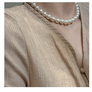 Gros plan d'un collier de perles en argent S925 porté avec une chemise en soie champagne