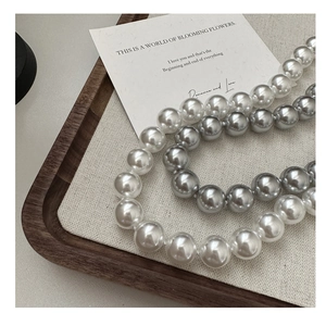 Close-up of S925 silver necklace featuring large white and grey pearls on wood