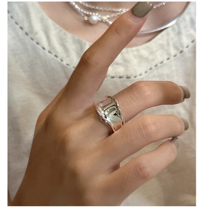 Dettaglio di un anello d'argento ondulato indossato con un maglione in maglia beige