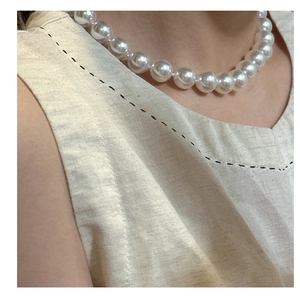 Close-up of a large 12mm white pearl pendant necklace on a beige linen fabric neckline