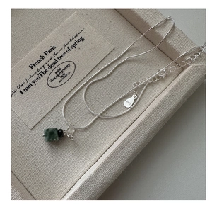 Macro detail of S925 sterling silver snake chain with green stone bow pendant and S925 stamp