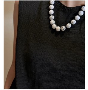 Detail of white marble bead necklace paired with black sleeveless knitted fabric texture