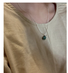 Detail of silver snake chain necklace with an irregular dark green raw stone pendant