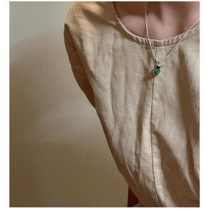 Detail of silver necklace with green gemstone pendant on model wearing linen shirt