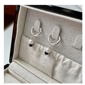 Détail de boucles d'oreilles en argent avec perle blanche dans un écrin texturé