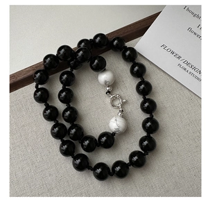 Detail of beaded necklace with black agate and white turquoise beads on linen fabric