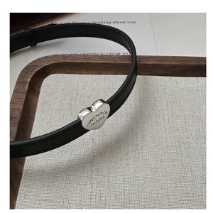 Macro detail of silver heart charm with engraving on black leather cord choker