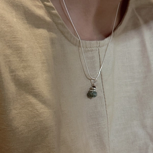 Collier Saturne en argent S925 avec pierres vertes et rouges sur fond de lin beige