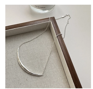 Close-up of S925 sterling silver smile necklace on beige woven tray with soft lighting