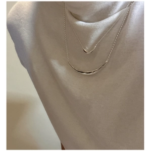 Close-up of layered S925 silver smile necklaces with crescent pendants on knitted fabric