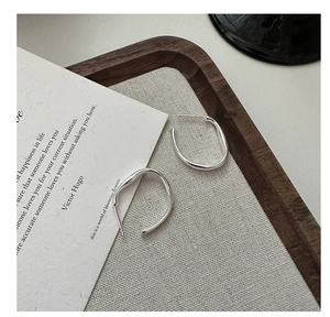 Macro view of S925 sterling silver C-shaped earrings on a rustic wood and fabric background